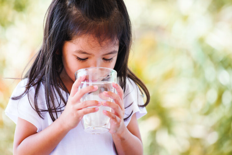 Cute asian little girl drinking fresh water from glass in vintage color tone