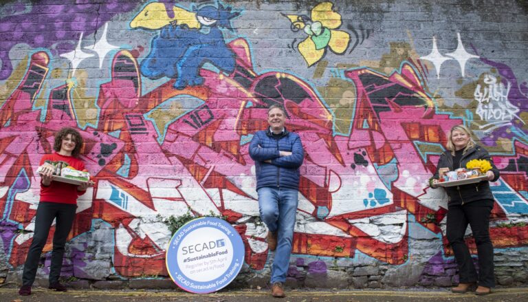 Trainers involved in the free sustainability programme by SECAD pose in front of a colourful wall