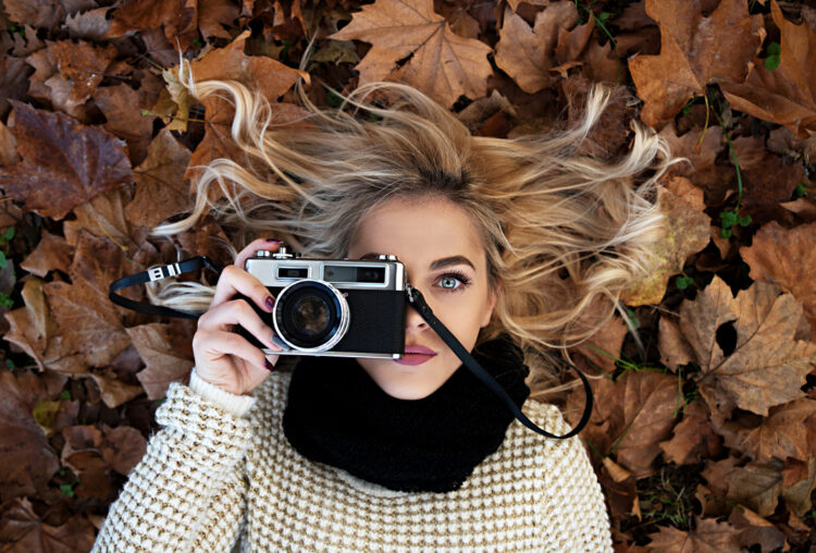 Beautiful girl laying in park with retro camera