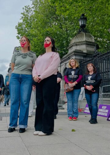 Posted by ROSA Socialist Feminism on Instagram, featuring Hazel Behan. Outside the Dáil, survivors stood with red handprints over their mouths and therapists stood with their hands tied. This is to symbolise the continued failure of the Minister for justice to listen to survivors and therapists